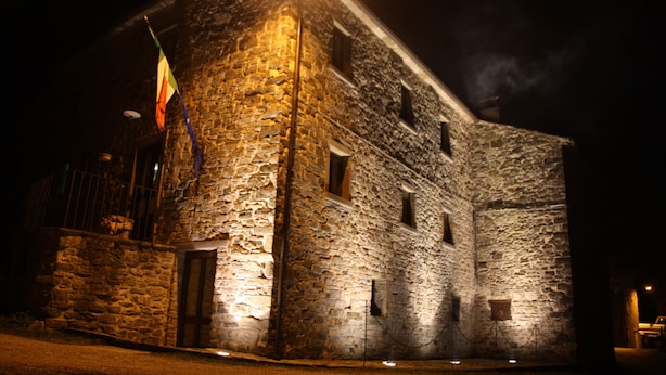 Ein Steinhaus mit Fahnenmast und Wimpel, beleuchtet durch eine einzelne Lichtquelle.