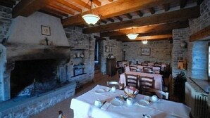 Ein rustikaler Essbereich mit Steinwänden, Holzbalken und einem Kamin. Die Tische sind mit Tellern und Besteck gedeckt.