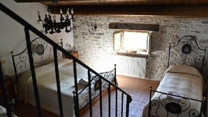 Ein rustikales Schlafzimmer mit Steinwand, Holzboden, schmiedeeisernem Bettgestell, einer Chandelieber und einem Fenster mit Aussicht.