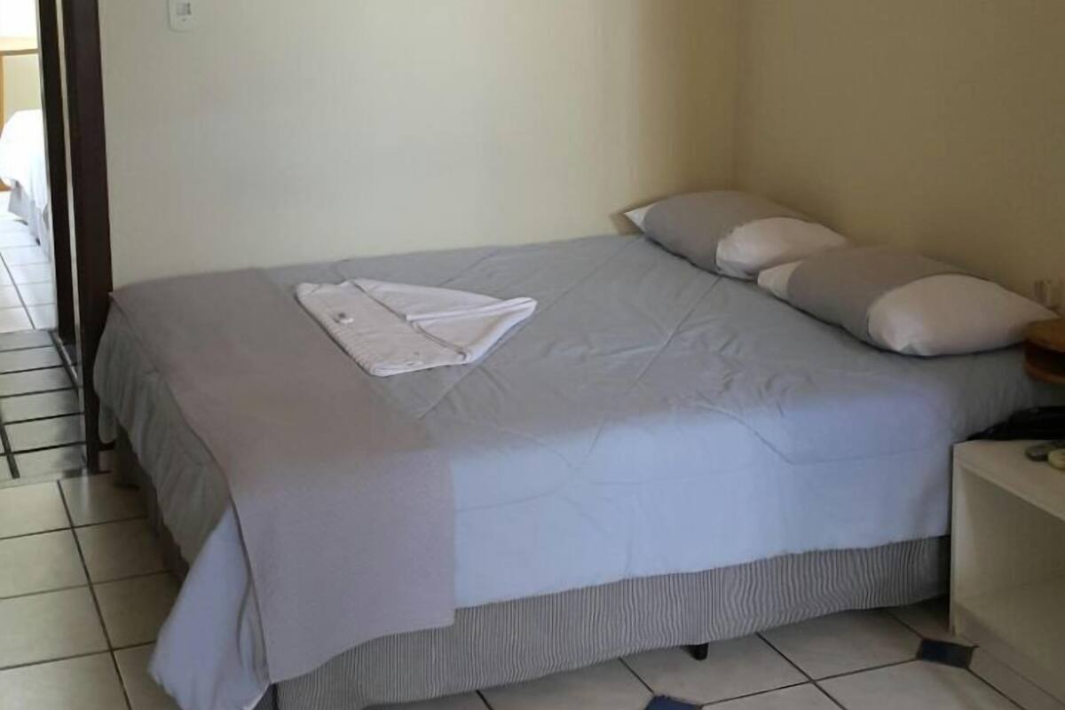 A bedroom with a bed, pillows, a nightstand, and a tiled floor.