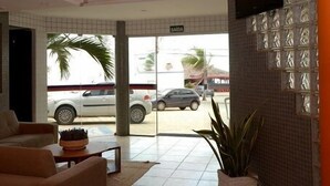 Vestíbulo de hotel con mostrador de recepción, zona de estar y vistas a coches aparcados afuera.