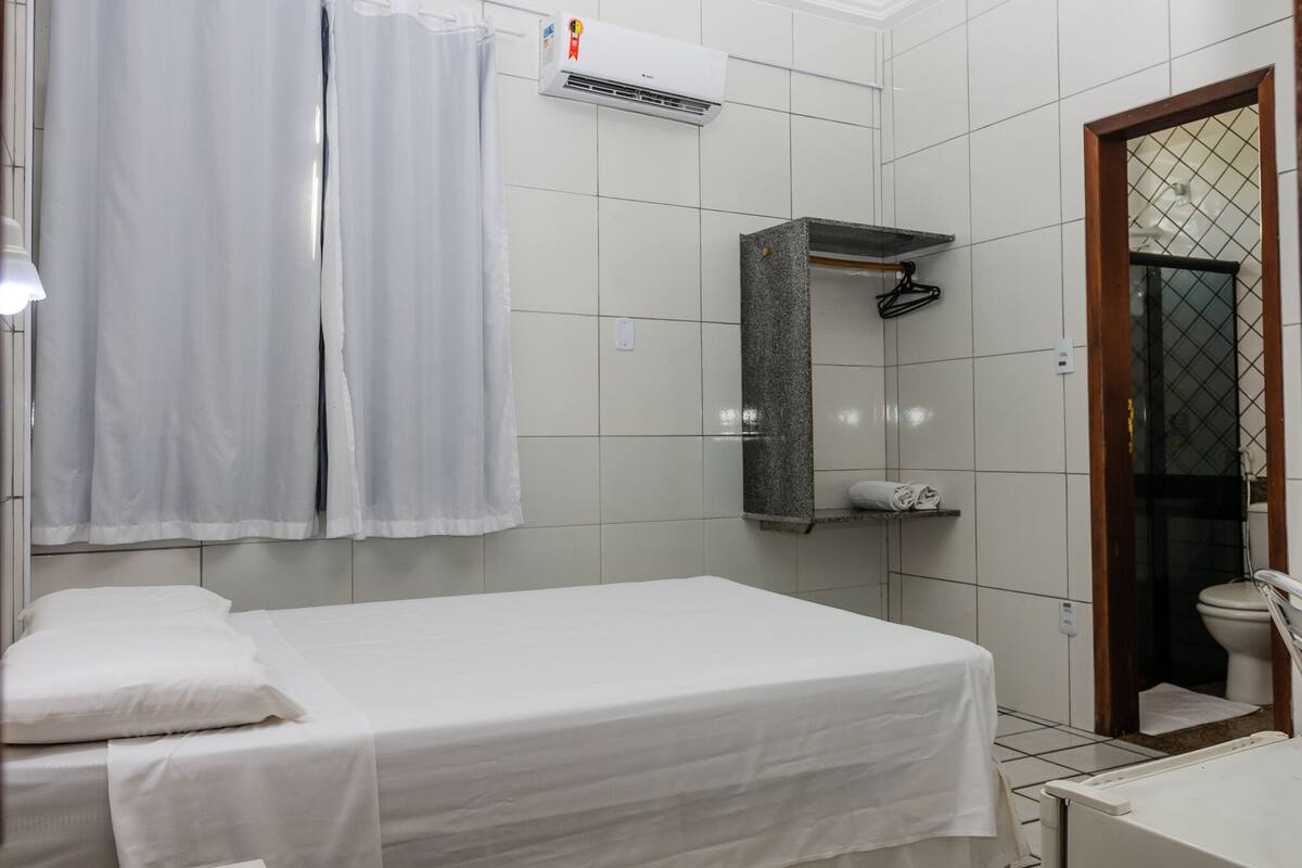 A clean, well-lit hotel room with a single bed, a shower area, and a small bathroom.