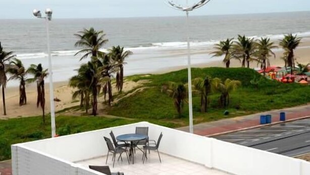 Una terraza con una mesa y sillas, con vista a una playa con palmeras y el océano.