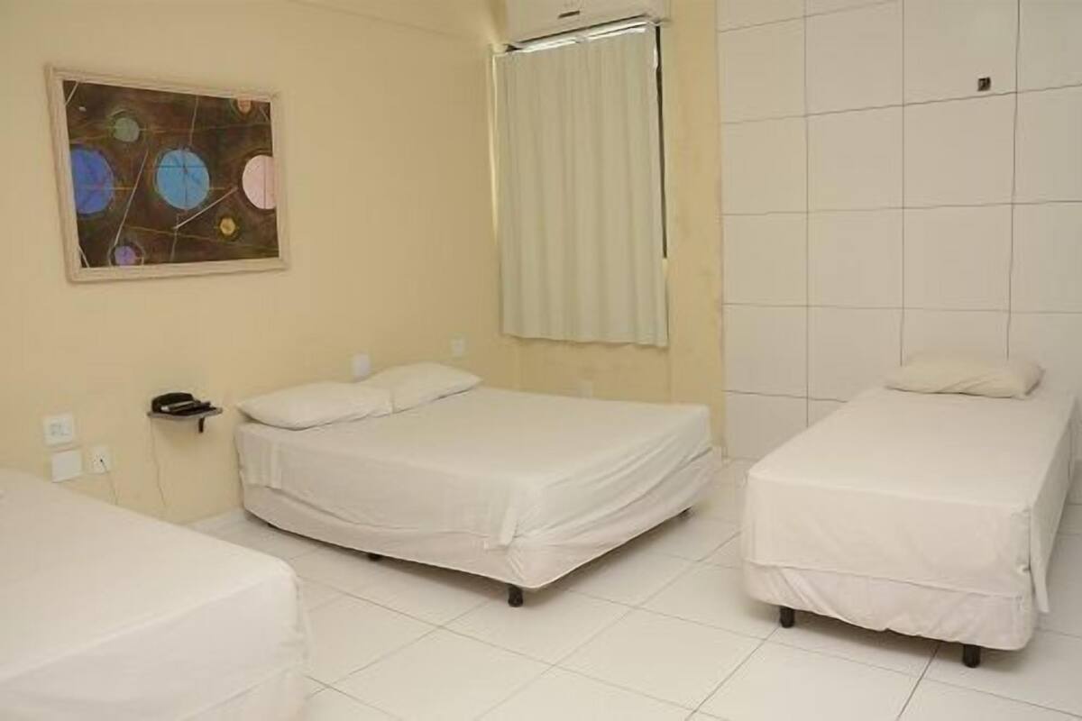 A hotel room with two beds, a painting on the wall, and a window with curtains.