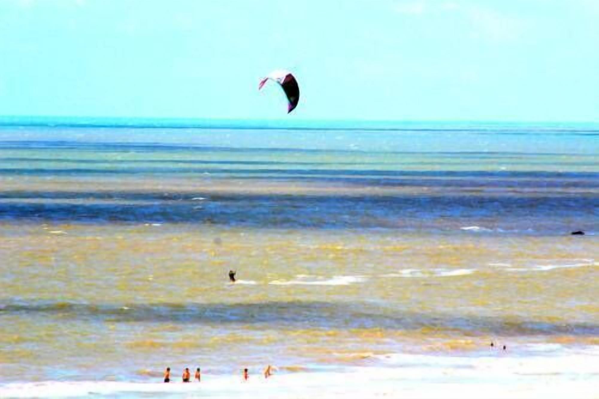A beach with people swimming and a person kite surfing.