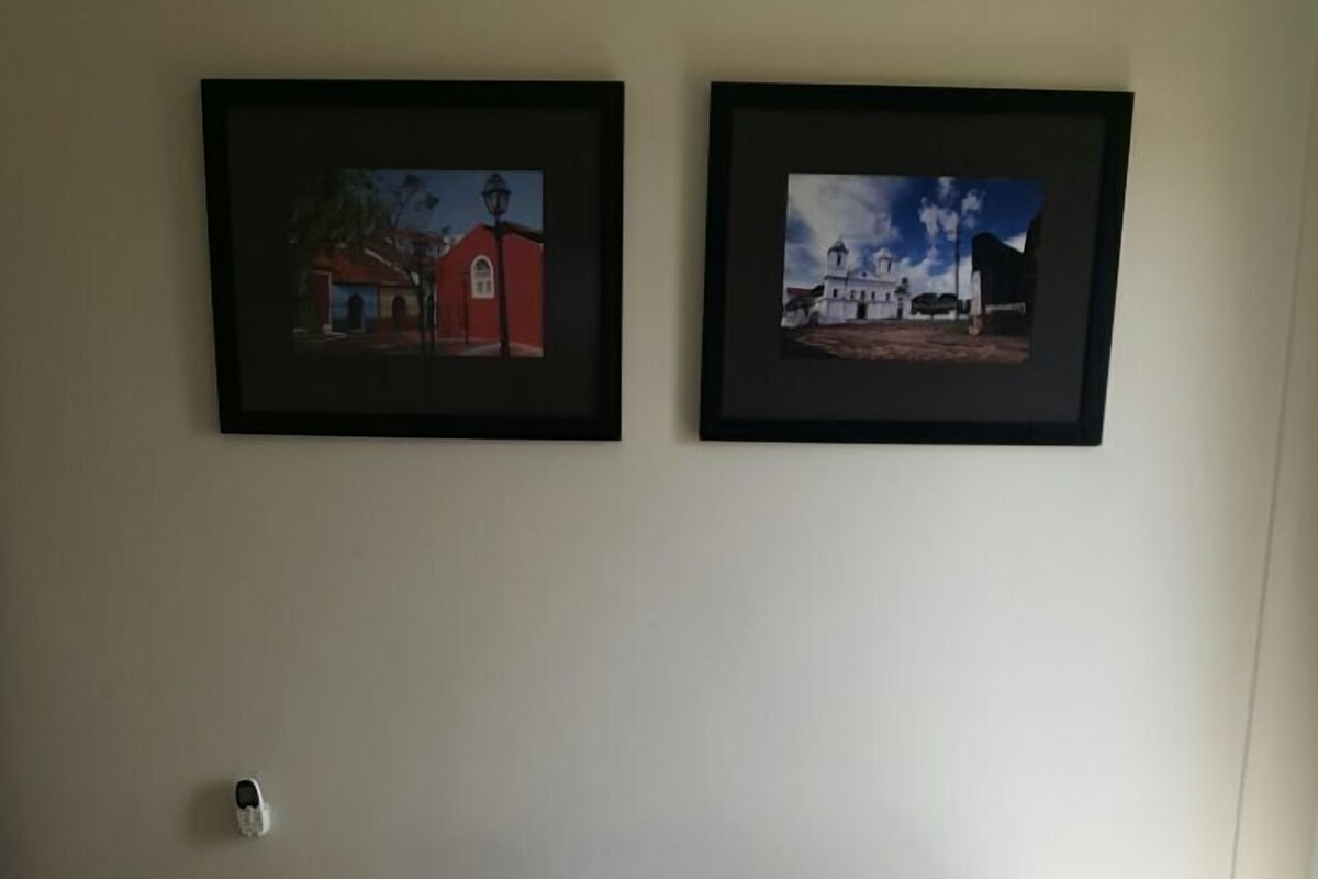A neatly made bed with towels, a bedside table with a phone, and two framed pictures on the wall.