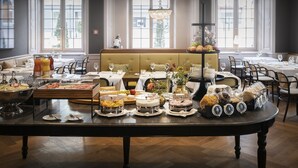 Una mesa de buffet con diferentes alimentos y bebidas en una habitación bien iluminada con ventanas grandes.