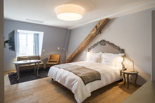 Un dormitorio con cama, escritorio, silla, televisor montado en la pared y estructura de vigas de madera.