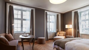 Una habitación de hotel con cama, sofá, sillón, mesita y lámpara.