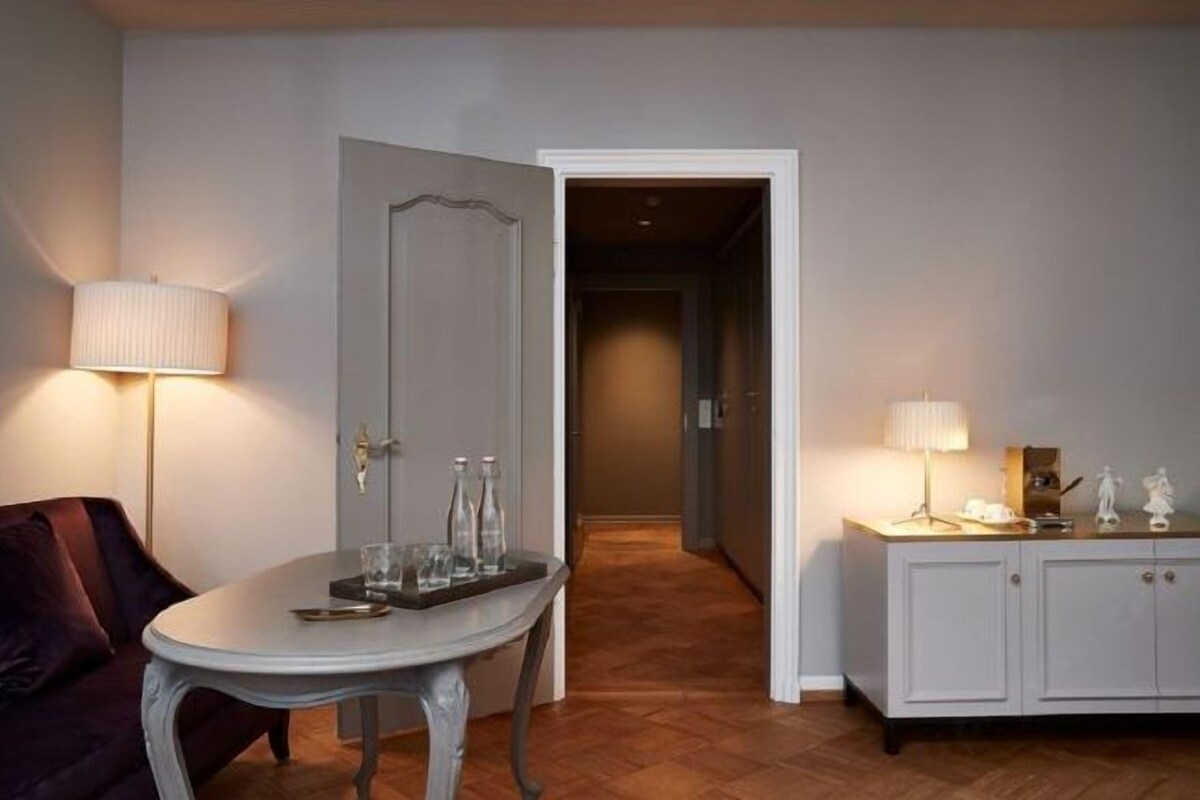 Una habitación con una mesa de comedor, un sofá, un aparador con objetos decorativos y una puerta que da a otra estancia.