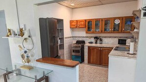 A kitchen with a refrigerator, stove, microwave, wooden cabinets, and a glass dining table. - Casa Little Italy (Tijeras)