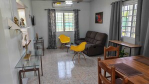 A living room with a sofa, two yellow chairs, a wooden dining table, and a TV. - Casa Little Italy (Tijeras)
