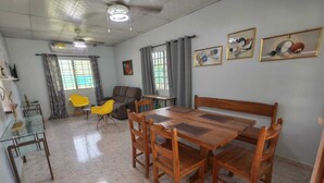 A dining area with a wooden table and chairs, a sofa, and a glass dining table. - Casa Little Italy (Tijeras)