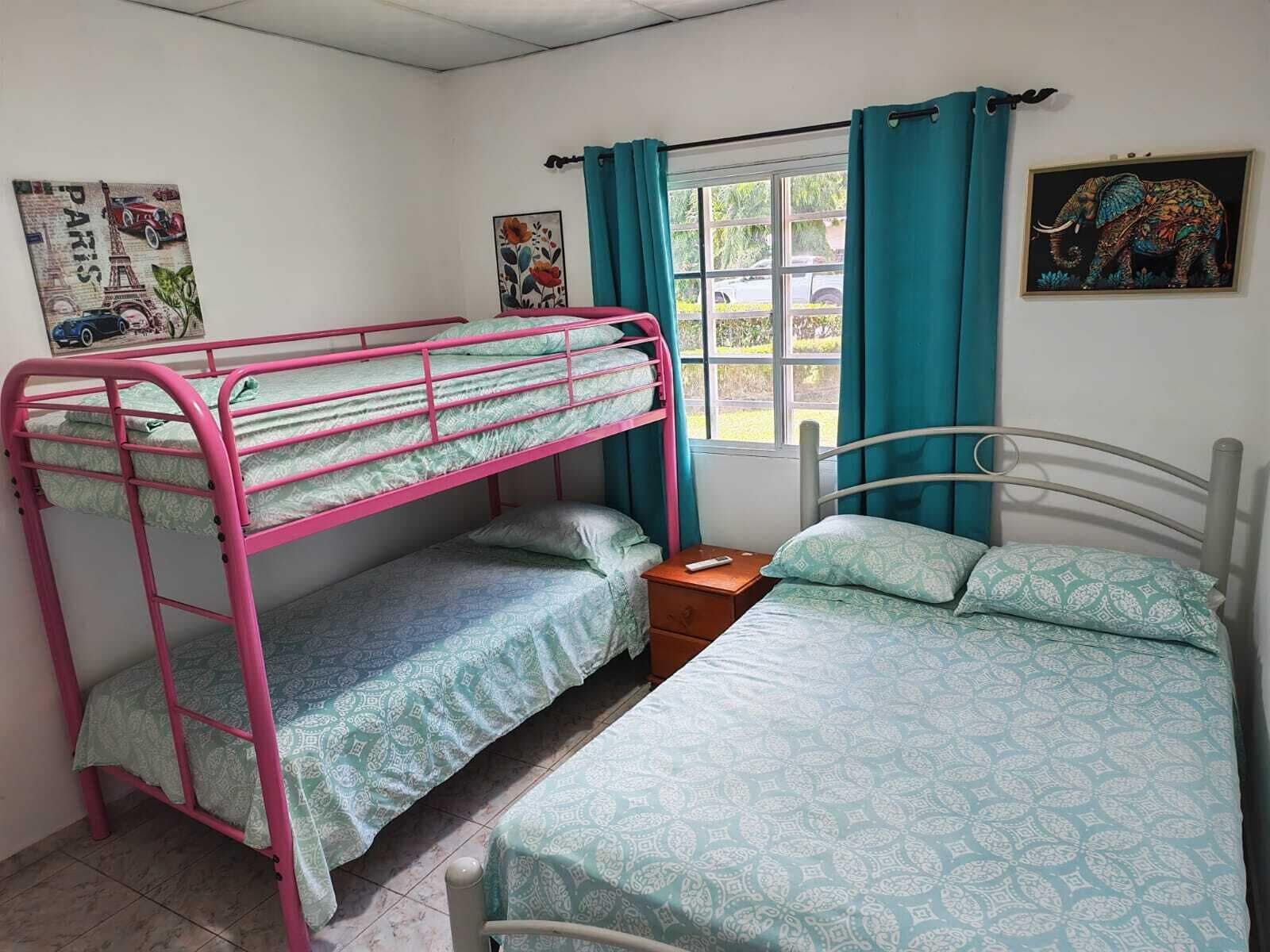 Een kamer met stapelbedden, een enkel bed, een raam met gordijnen en wanddecoratie.