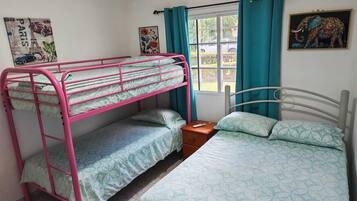 Een kamer met stapelbedden, een enkel bed, een raam met gordijnen en wanddecoratie.
