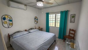 A bedroom with a bed, a ceiling fan, a window with curtains, a chair, and a wall-mounted air conditioner. - Casa Little Italy (Tijeras)
