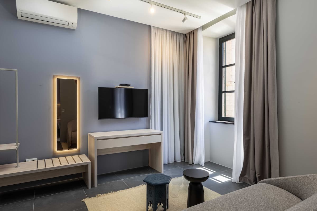 Ein modernes Schlafzimmer mit einem großen Bett, einem Nachttisch, einem an der Wand montierten Fernseher und einem Fenster mit Vorhängen.