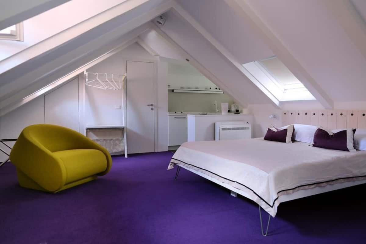 Ein Schlafzimmer mit einem Bett, einem gelben Sessel, einer Küchenzeile und einem Oberlicht.