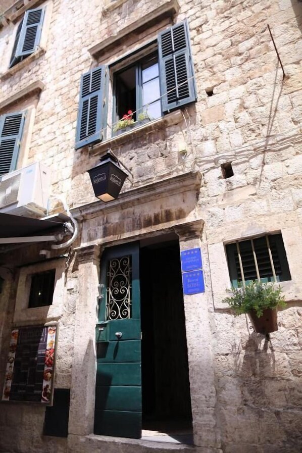 Un bâtiment en pierre avec une porte verte, une enseigne indiquant un restaurant et un pot de fleurs sur la droite.