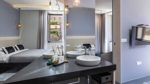 Moderni hotellihuone, jossa on suuri sänky, kaksi pyöreää pesuallasta, taulutelevisio ja suuri ikkuna, josta avautuu näkymä vehreään maisemaan.