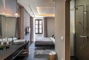 Casa de banho moderna com um espelho grande, uma luminária redonda, um chuveiro e uma cama ao fundo.