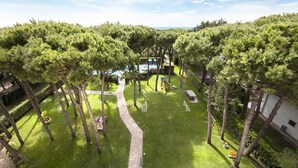 A well-maintained garden with a pathway, a children's play area, and a pool. - Aparthotel la Pineta (Jesolo)