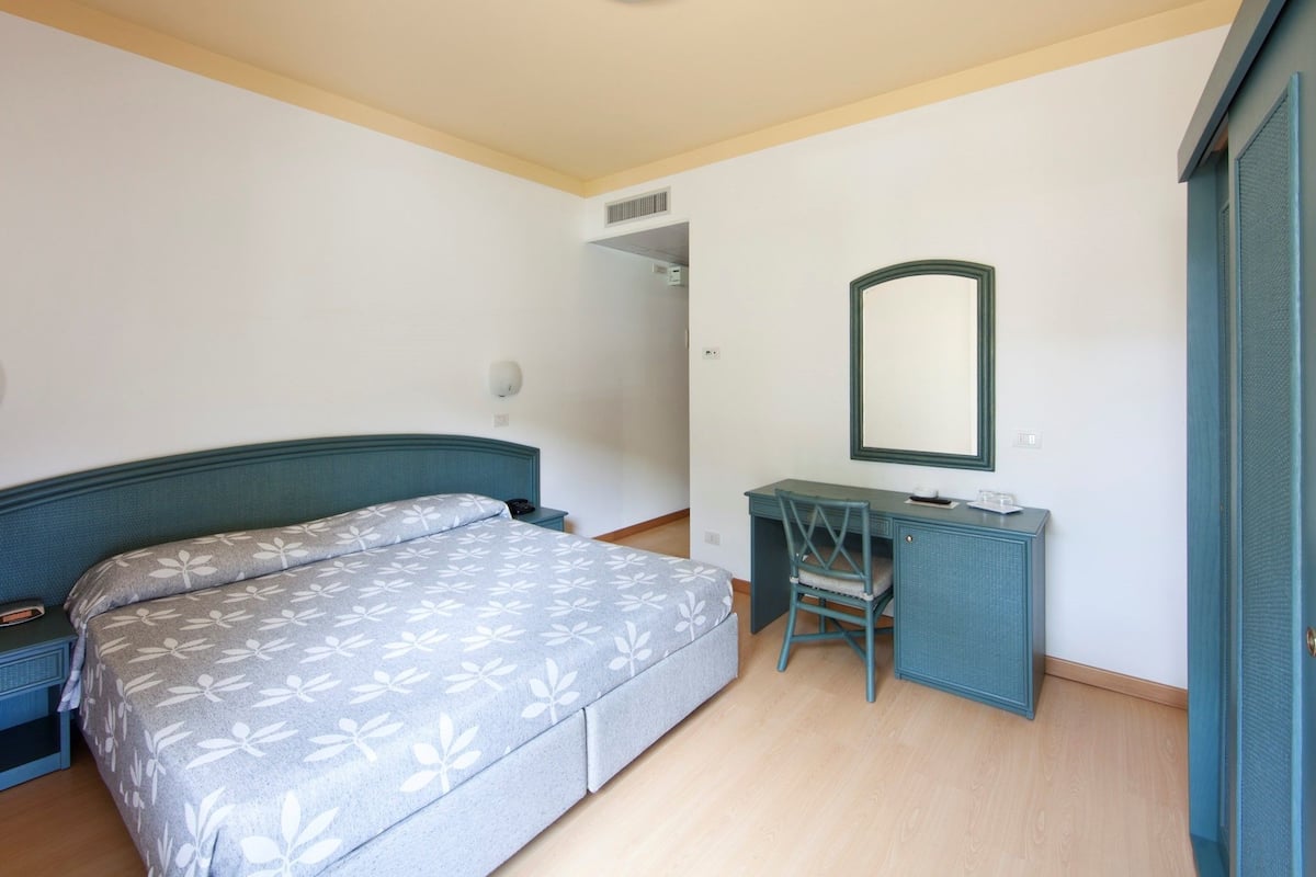 A bedroom with a bed, a desk, and a mirror.