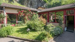 A traditional building with a red roof and a garden with various plants and flowers. - Hôtel La Cascade (Saint-Genis-les-Ollieres)