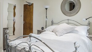 A neatly made bed with white linens, a round mirror on the wall, and a wooden door. - Burlington Hotel Hull City Centre (Hull)