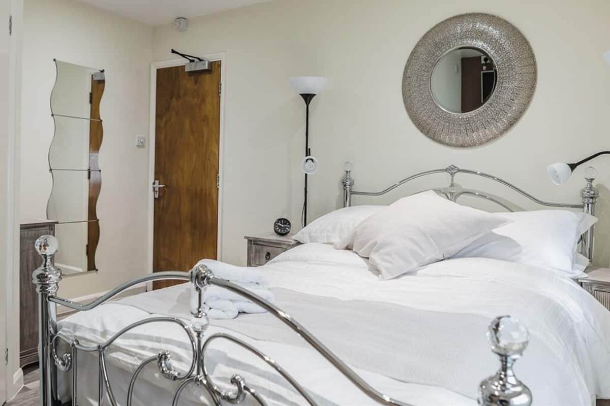 Un lit bien fait, avec du linge de lit blanc, un miroir rond accroché au mur et une porte en bois.