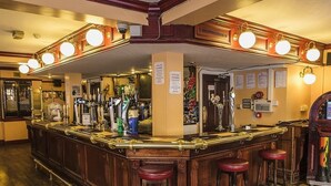A bar area with a wooden counter, bar stools, and a variety of bottles and glasses. - Burlington Hotel Hull City Centre (Hull)