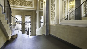 A grand hallway with a staircase, ornate wall patterns, and a large column. - Bonavista Apartments - Pedrera (Barcelona)