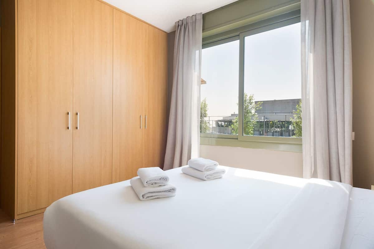 Une chambre d’hôtel avec un grand lit, une armoire en bois et une vue sur les immeubles par la fenêtre.