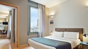 A modern hotel room with a large bed, a view of the city, and a small desk with a lamp. - Bonavista Apartments - Pedrera (Barcelona)