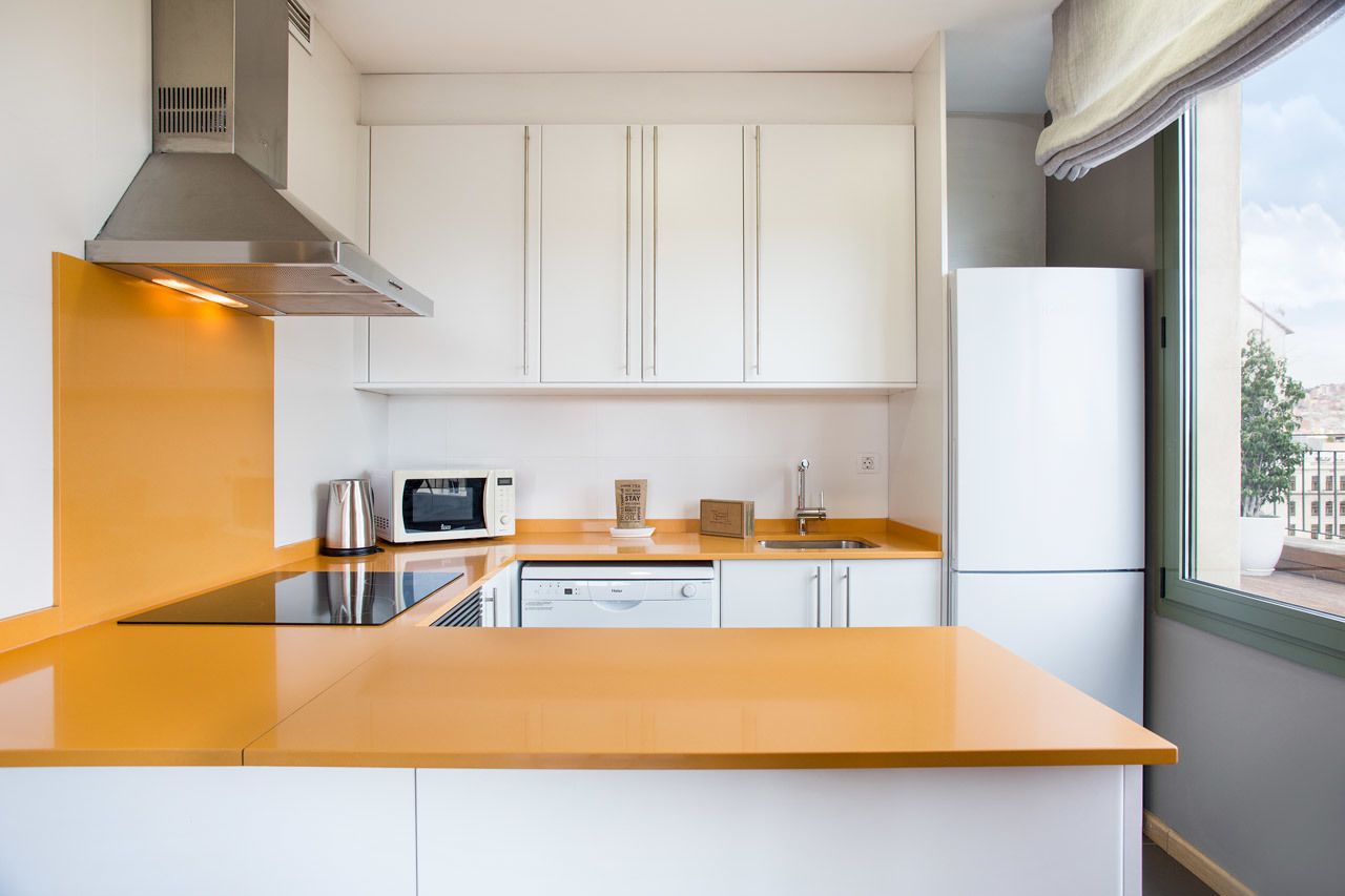 Una cocina moderna con armarios blancos, una campana extractora de acero inoxidable, un microondas y un lavavajillas.