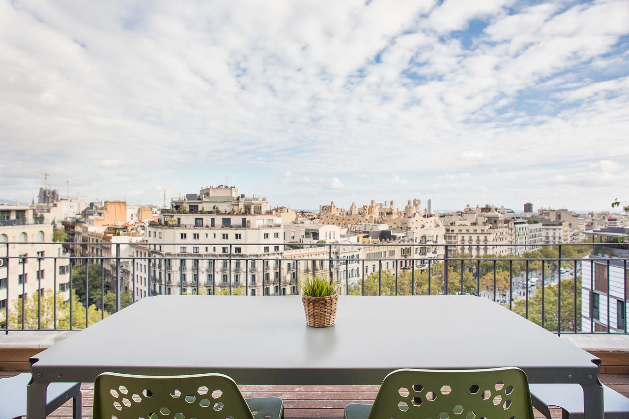 Un balcón con mesa y sillas, con vistas a un paisaje urbano con diversos edificios.