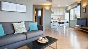 A modern living room with a grey sofa, a coffee table, and a dining area with a table and chairs. - Bonavista Apartments - Pedrera (Barcelona)