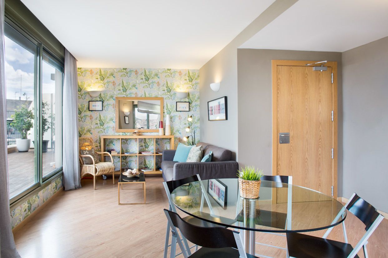 Ein modernes Wohnzimmer mit einem Glastisch, einer Couch und einem Couchtisch. Es gibt ein großes Fenster, eine Tür und einen wandmontierten Spiegel.