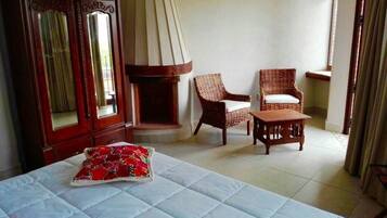 Una habitación de hotel con una cama, dos sillones de mimbre, un armario de madera y una pequeña mesa.