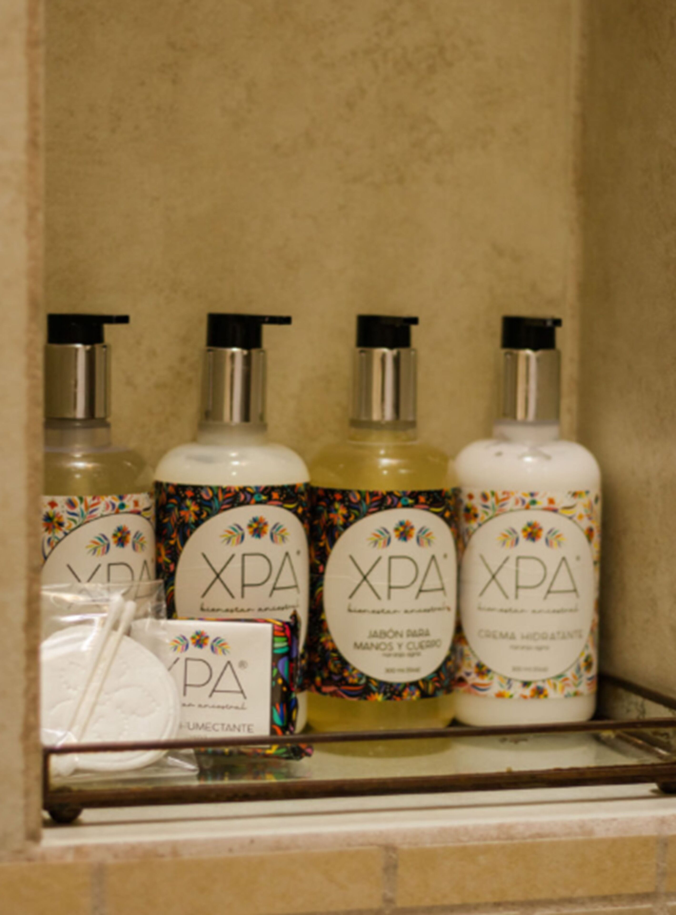 A shelf with three bottles of XPA hand and body care products, a white cloth, and a box.