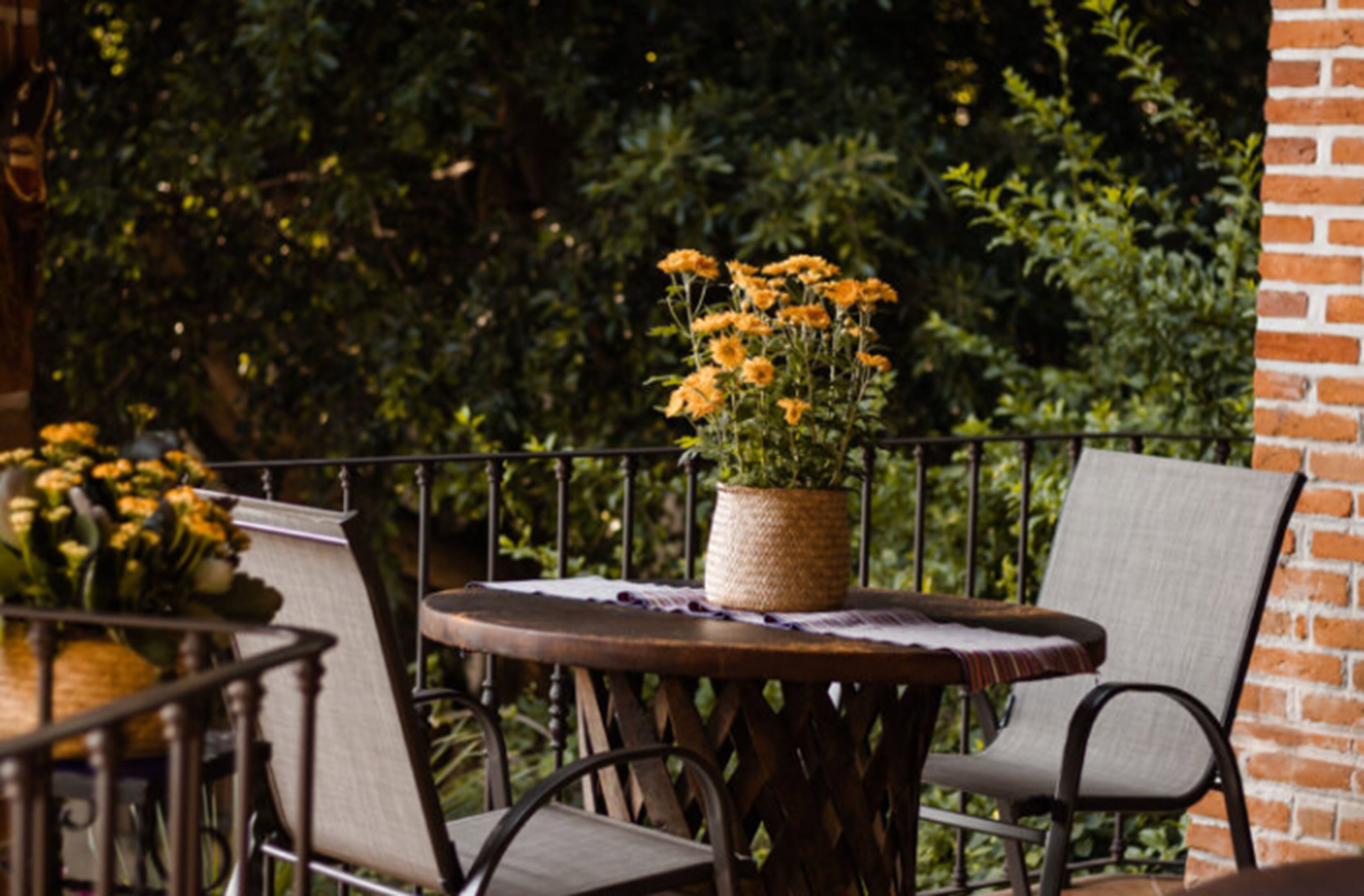 A round table with a woven basket of yellow flowers, two chairs, and a brick wall in the background.