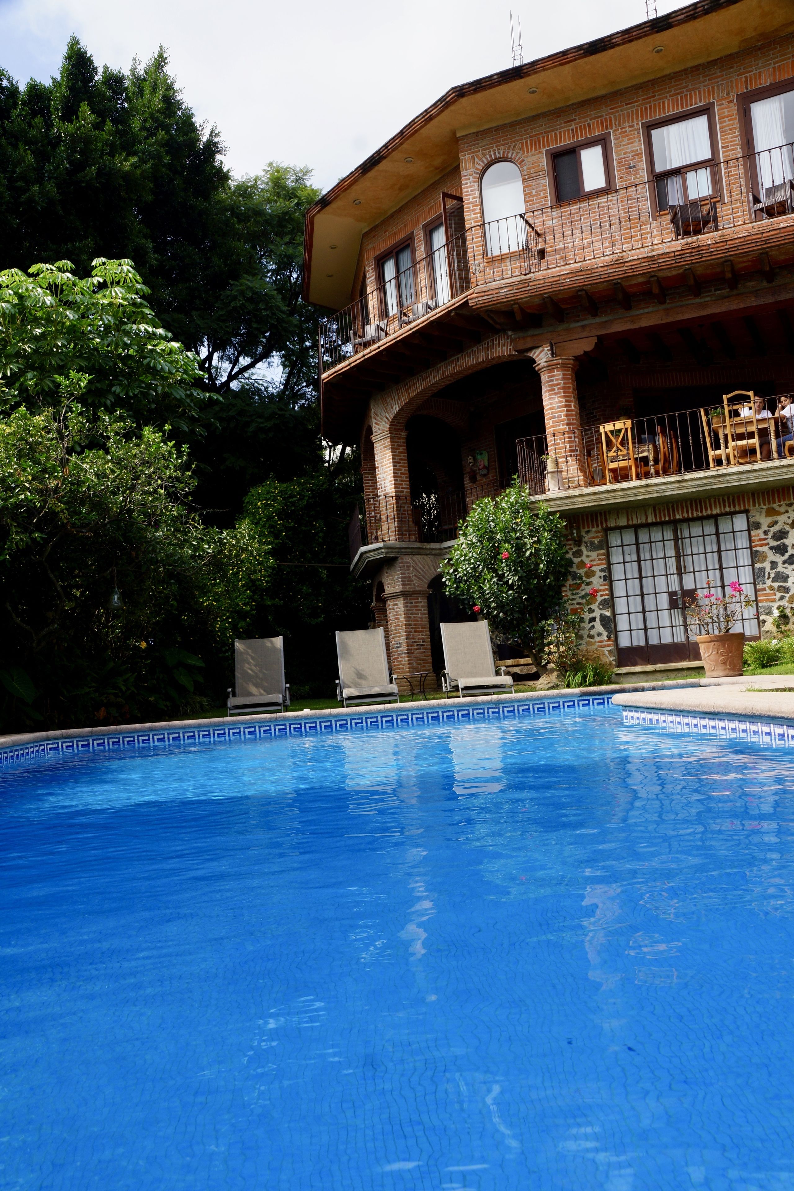 A two-story house with a swimming pool, a balcony with outdoor furniture, and a garden.