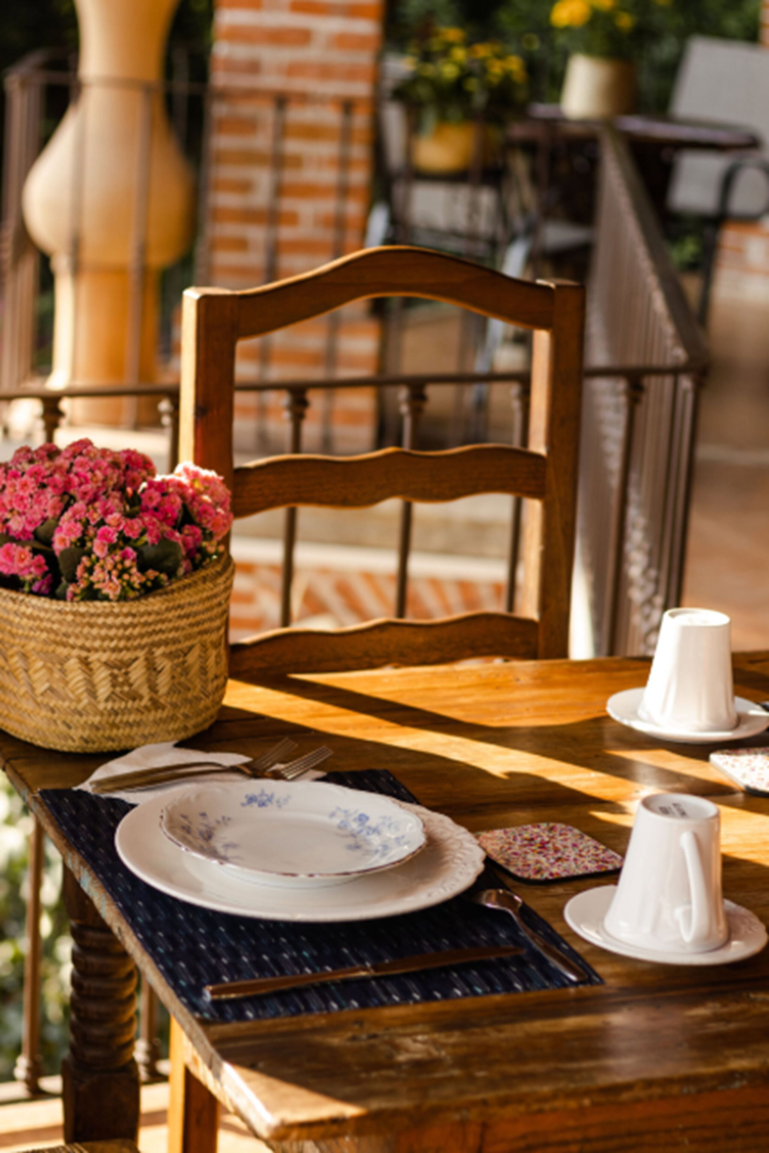 Une table de salle à manger en bois, sur laquelle se trouve un panier tressé rempli de fleurs, une assiette, une tasse et un pichet.
