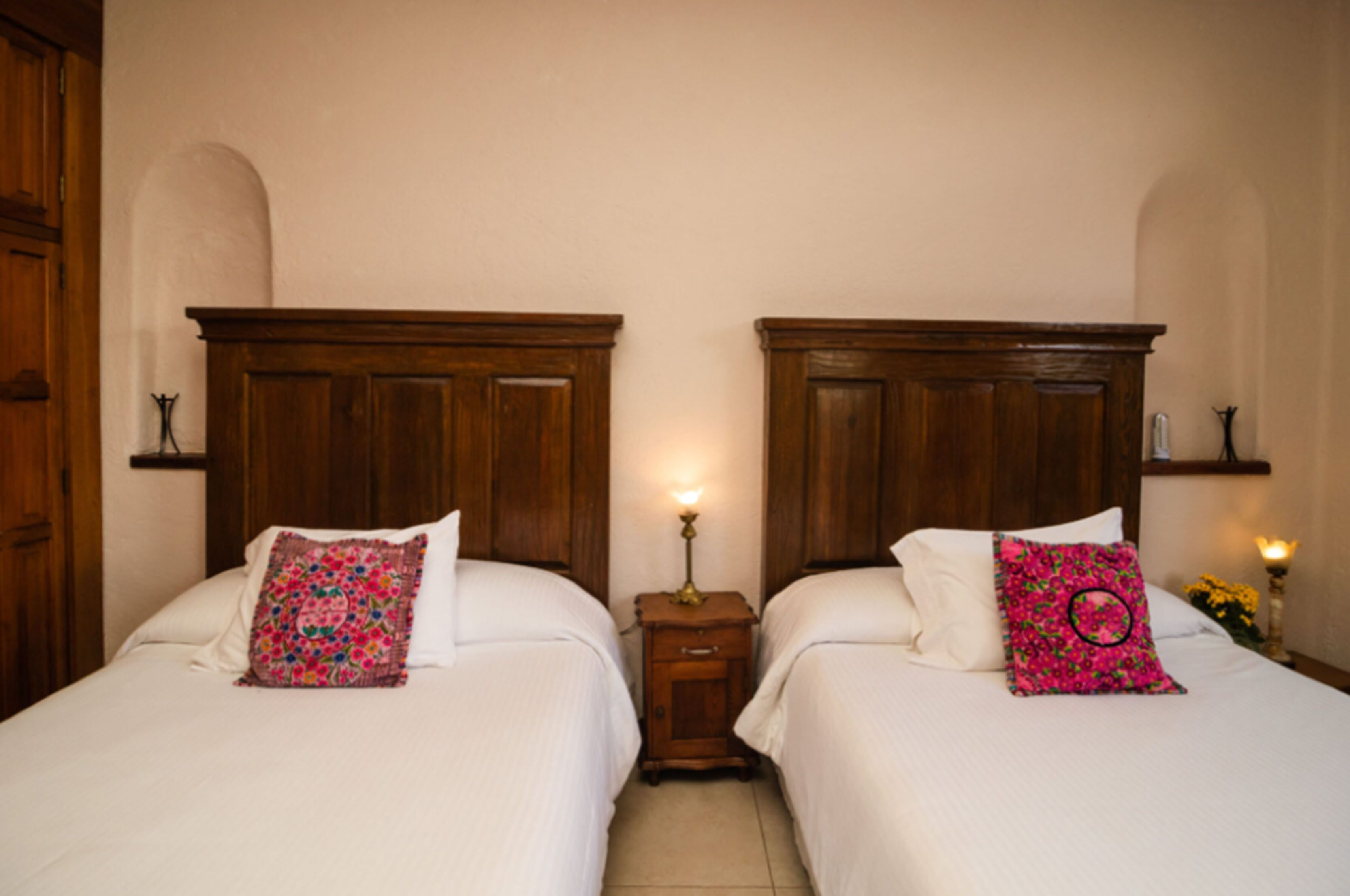A double room with two beds, each with a wooden headboard, a small bedside table, and a lamp.