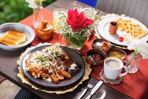 A table set with a plate of food, a cup of coffee, and a vase with flowers.