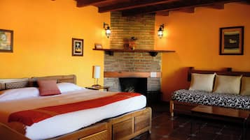 A bedroom with a large bed, a wooden bench, a fireplace, and wall-mounted lights.