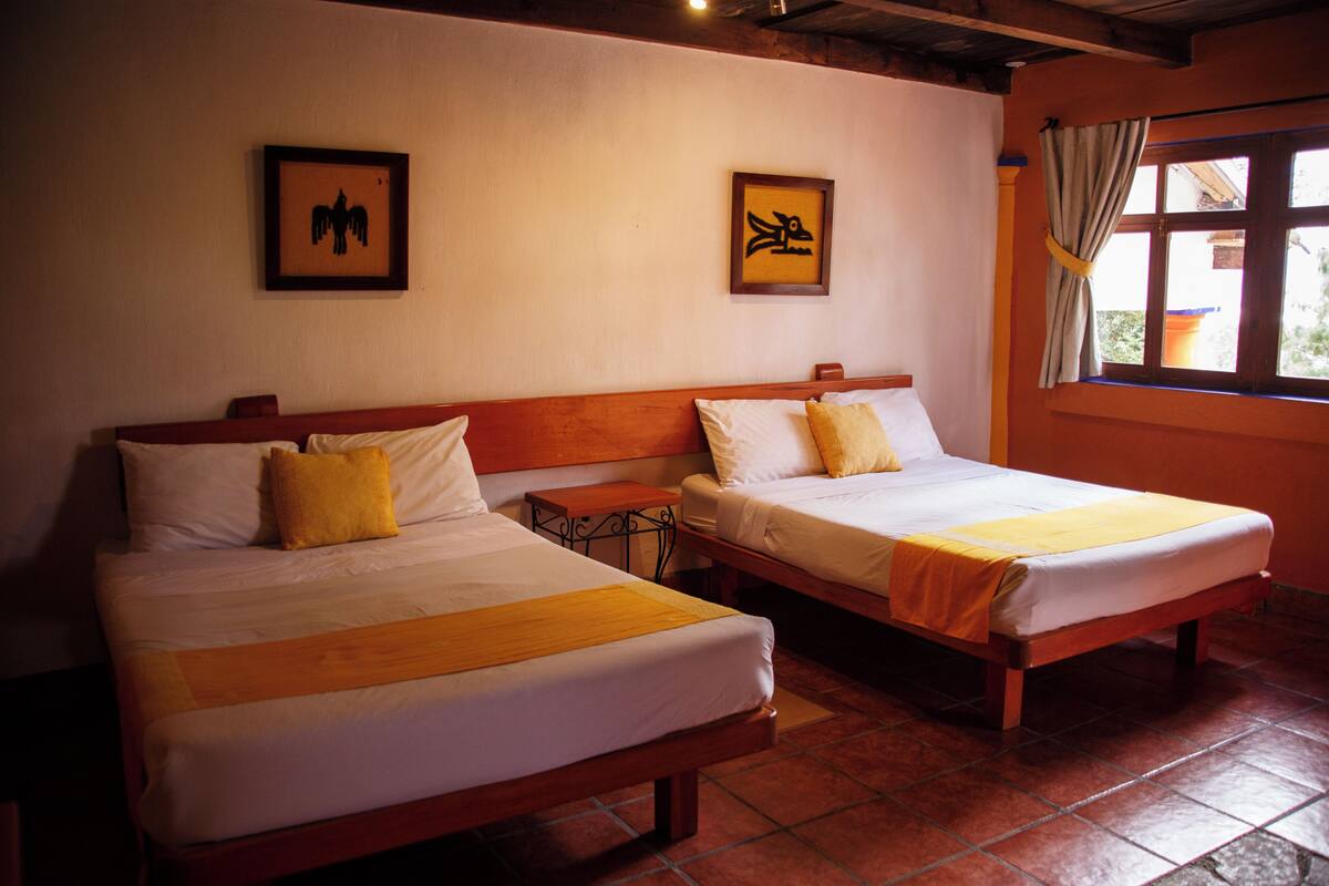 Two single beds with wooden frames and white bedding, a small bedside table, and a window with curtains.