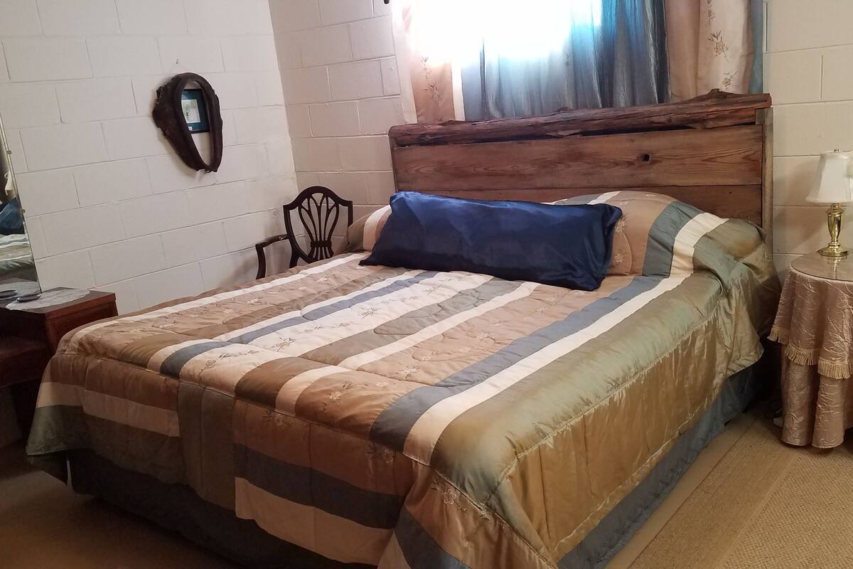 Ein Schlafzimmer mit einem Bett, einem hölzernen Kopfteil, einem Nachttisch mit Lampe, einer Uhr und einem Spiegel an der Wand.