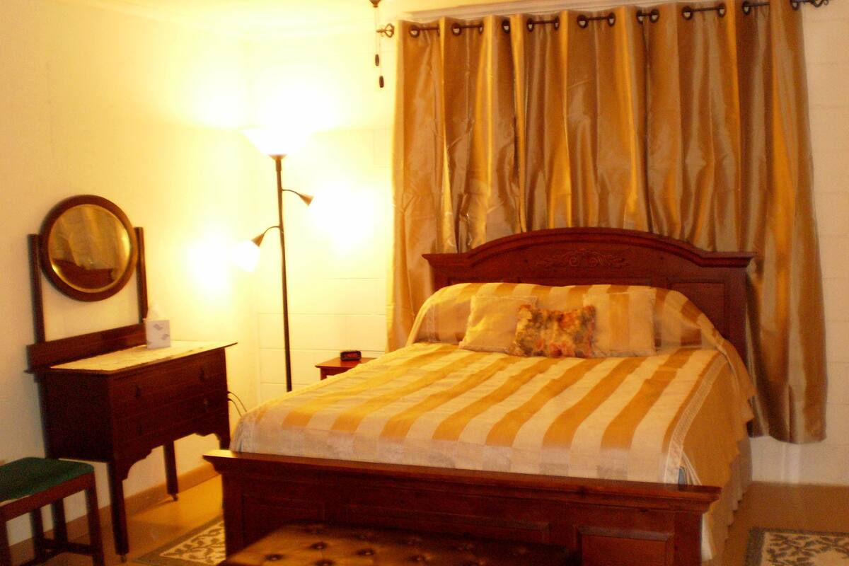 Ein Schlafzimmer mit einem hölzernen Bett, einem Nachttisch, einem Spiegel und einer Stehlampe.