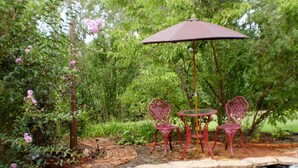 Un jardín con un estanque, sillas de metal rojas y una mesa bajo un paraguas morado.